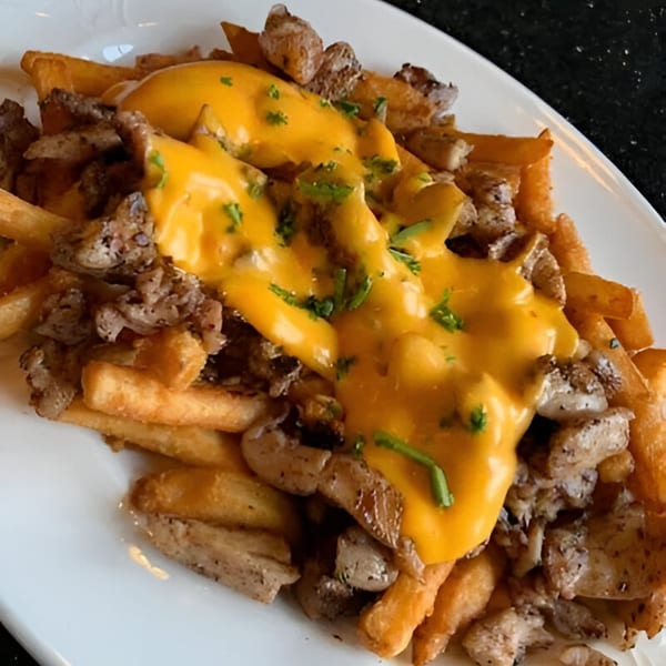 Golden french fries topped with sliced meat, melted cheese sauce, and fresh parsley.