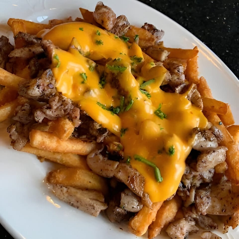 Golden french fries topped with sliced meat, melted cheese sauce, and fresh parsley.