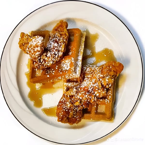 Chicken and waffles drizzled with syrup and powdered sugar on a white plate.