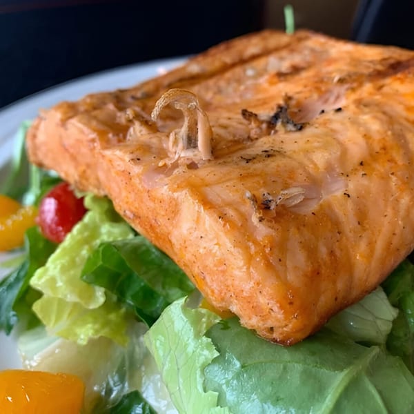 Grilled salmon fillet with crispy skin, served on a bed of fresh green salad with cherry tomatoes.