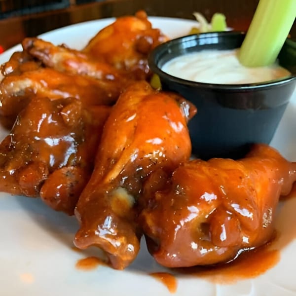 Spicy chicken wings with a side of ranch dressing and a celery stick on a white plate.