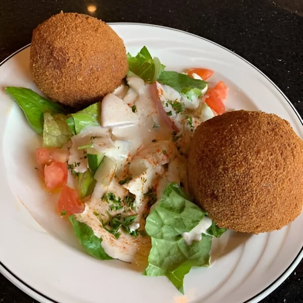 Two large, round, breaded kibbeh balls on a bed of fresh salad with dressing.