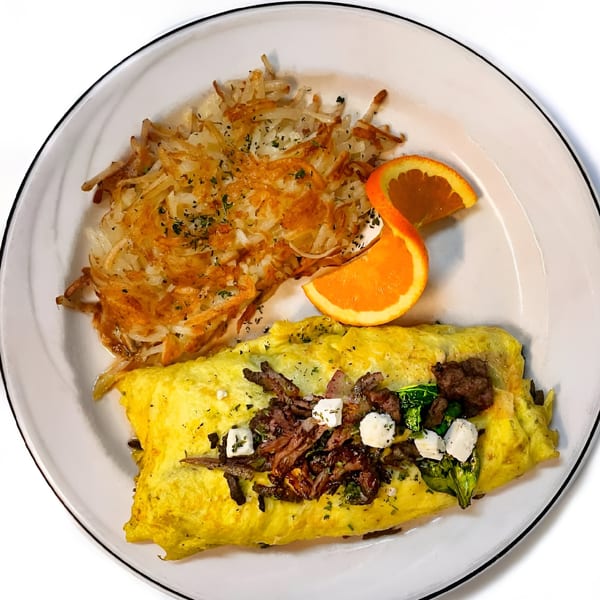 Middle-eastern omelet with hash browns and an orange slice on a white plate.